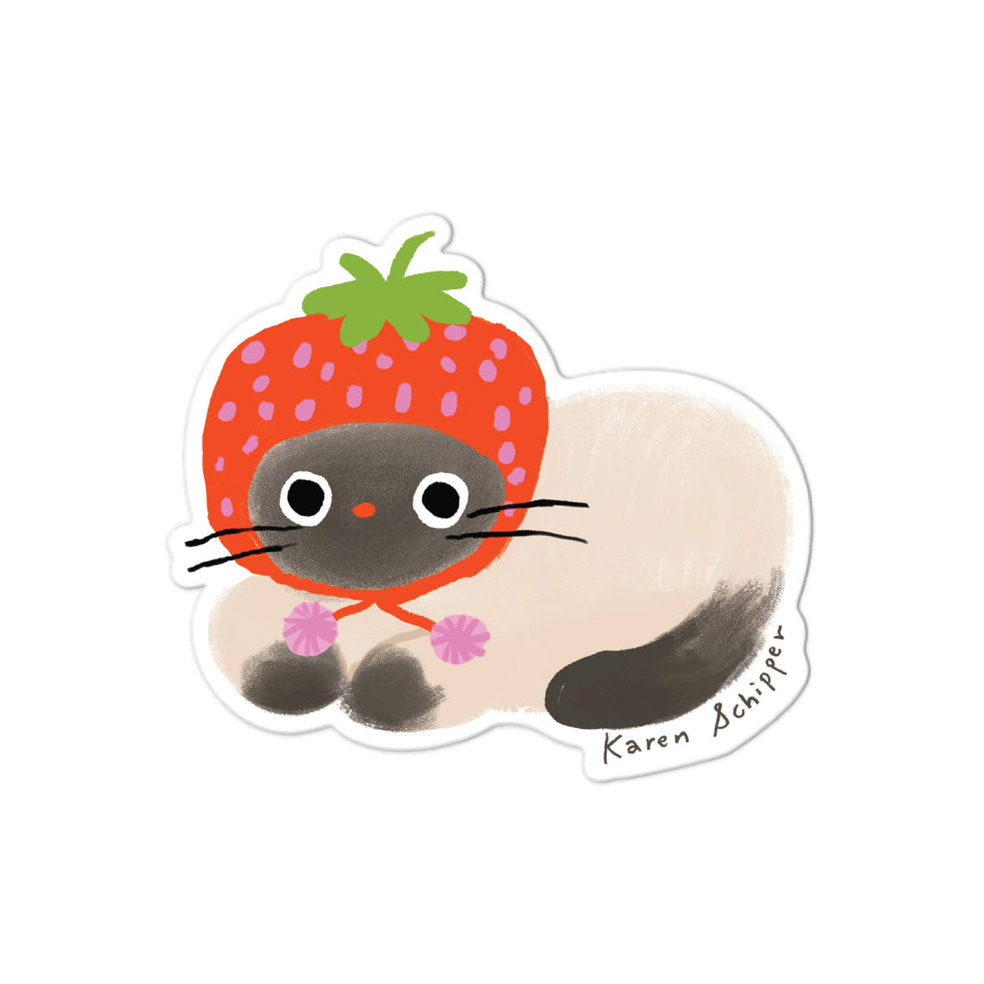 A die-cut sticker featuring a cute cartoon cat wearing a red strawberry bonnet, with a cream-colored body and tail.