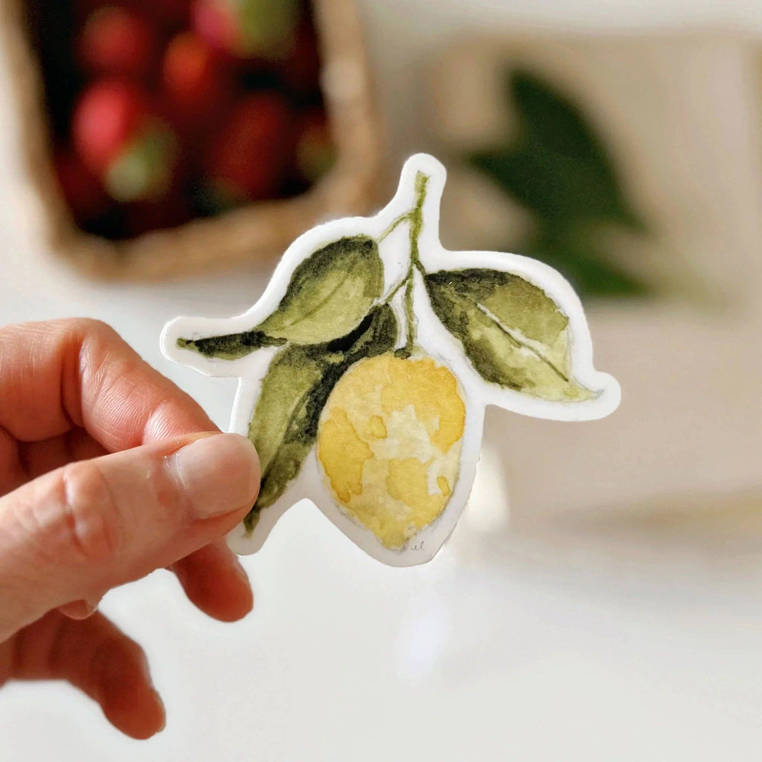 Hand holding sticker of a lemon with three leaves.