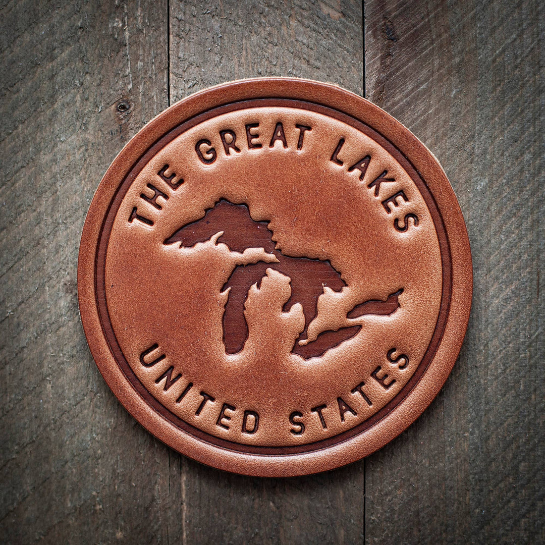Round leather coaster  with a silhouette of the Great Lakes and the words 'THE GREAT LAKES UNITED STATES' around the circumference.