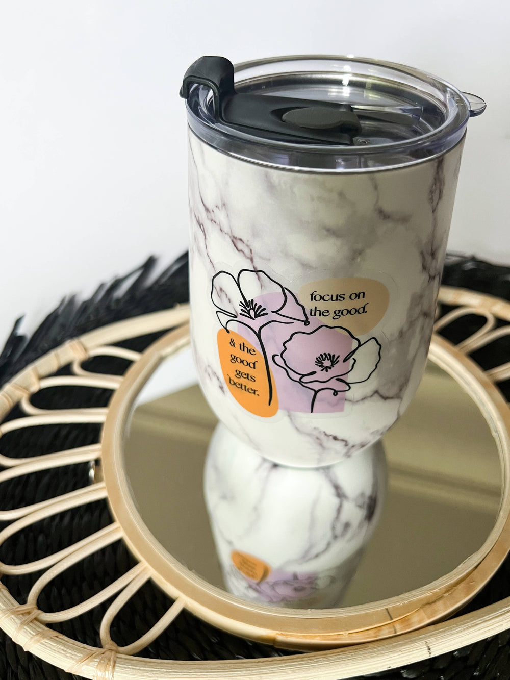 Sticker on a marble-patterned insulated tumbler with a clear lid and flip spout, displayed on a round mirror tray.