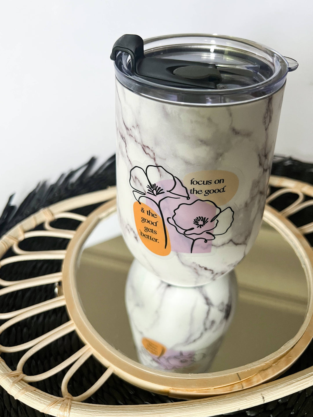 Sticker on a marble-patterned insulated tumbler with a clear lid and flip spout, displayed on a round mirror tray.