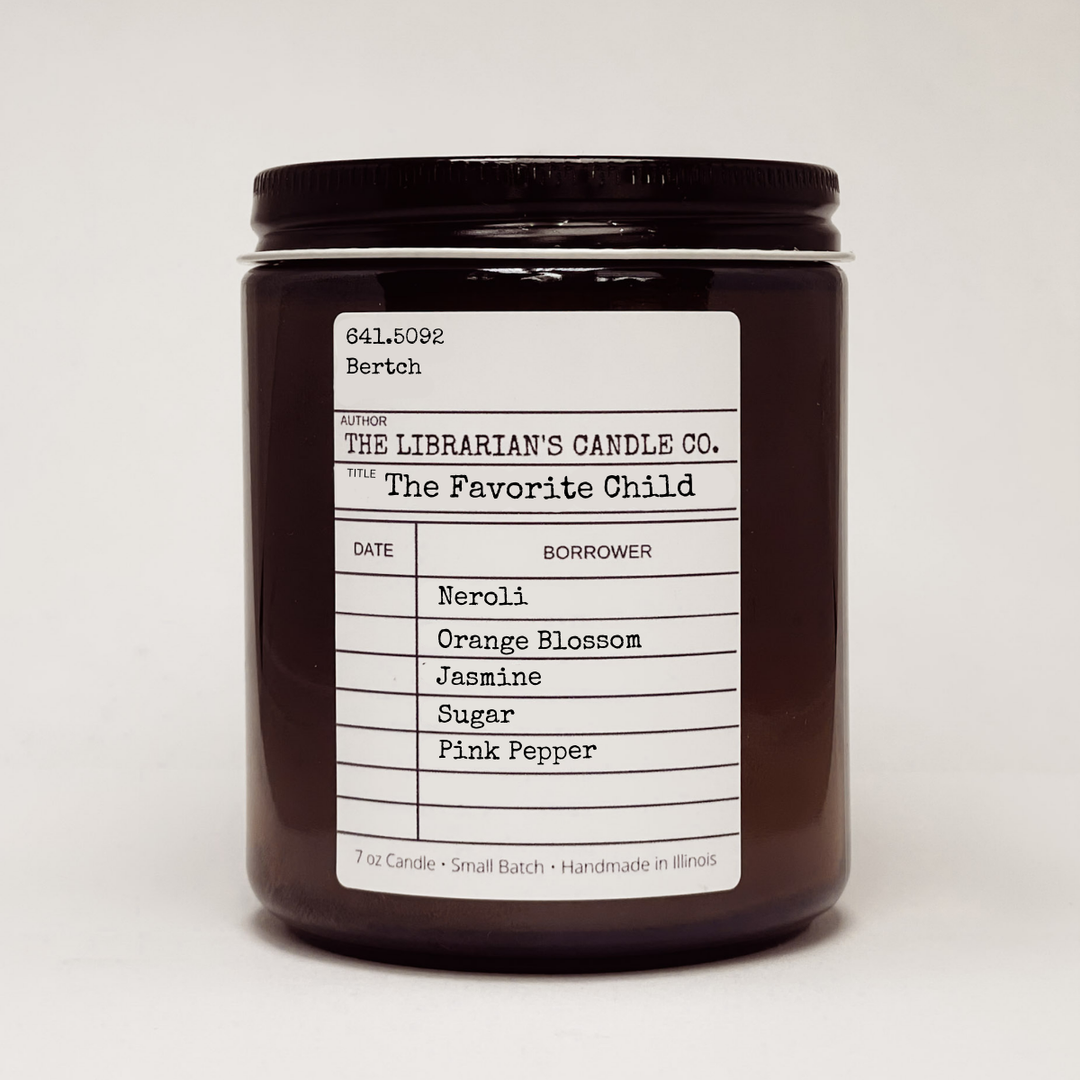 Candle jar with a label in the design of a library due date slip for the book 'The Favorite Chilc' detailing the candles scent notes: Neroli, Orange Blossom, Jasmine, Sugar, and Pink Pepper