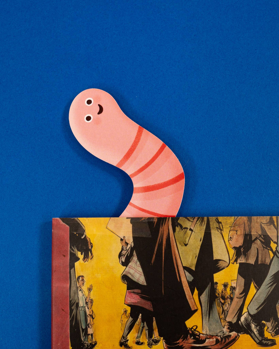 Bookmark in the shape of a cartoonish pink worm-like character sticking out of a book.