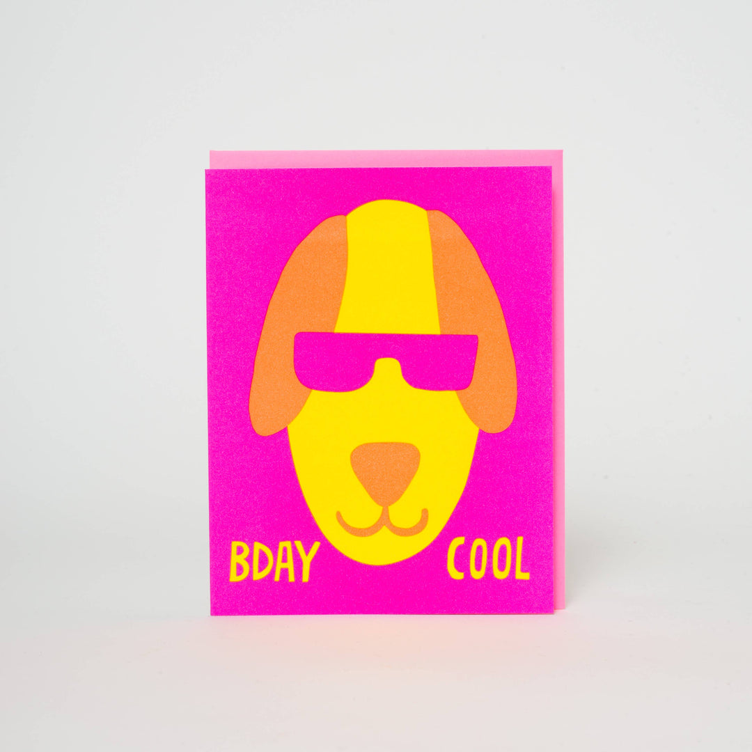 Drawing of yellow dog with brown ears and magenta sunglasses on magenta cardstock with text at bottom in yellow.