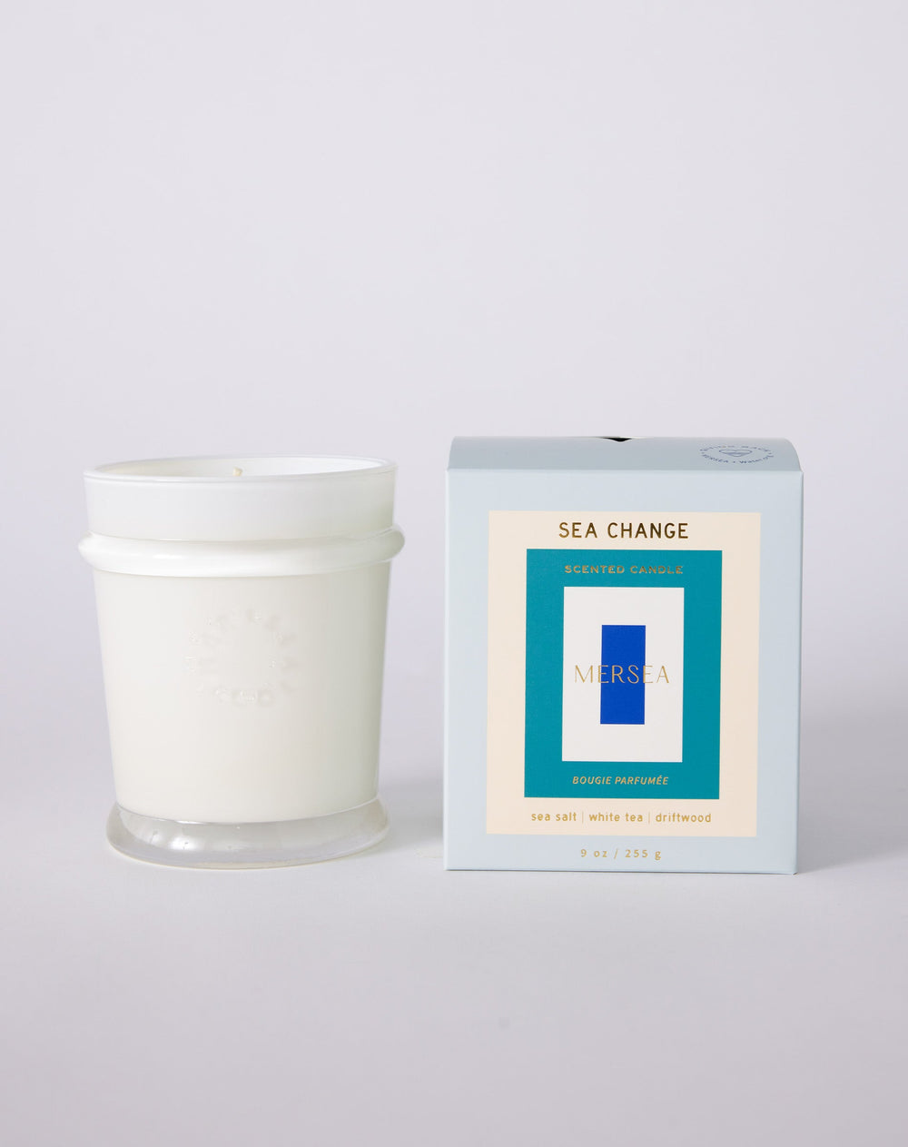White glass jar sits beside its light gray packaging box. The box has concentric rectangles in off-white, teal, white and blue, and is  labeled 'SEA CHANGE' and the brand 'MERSEA' in gold.