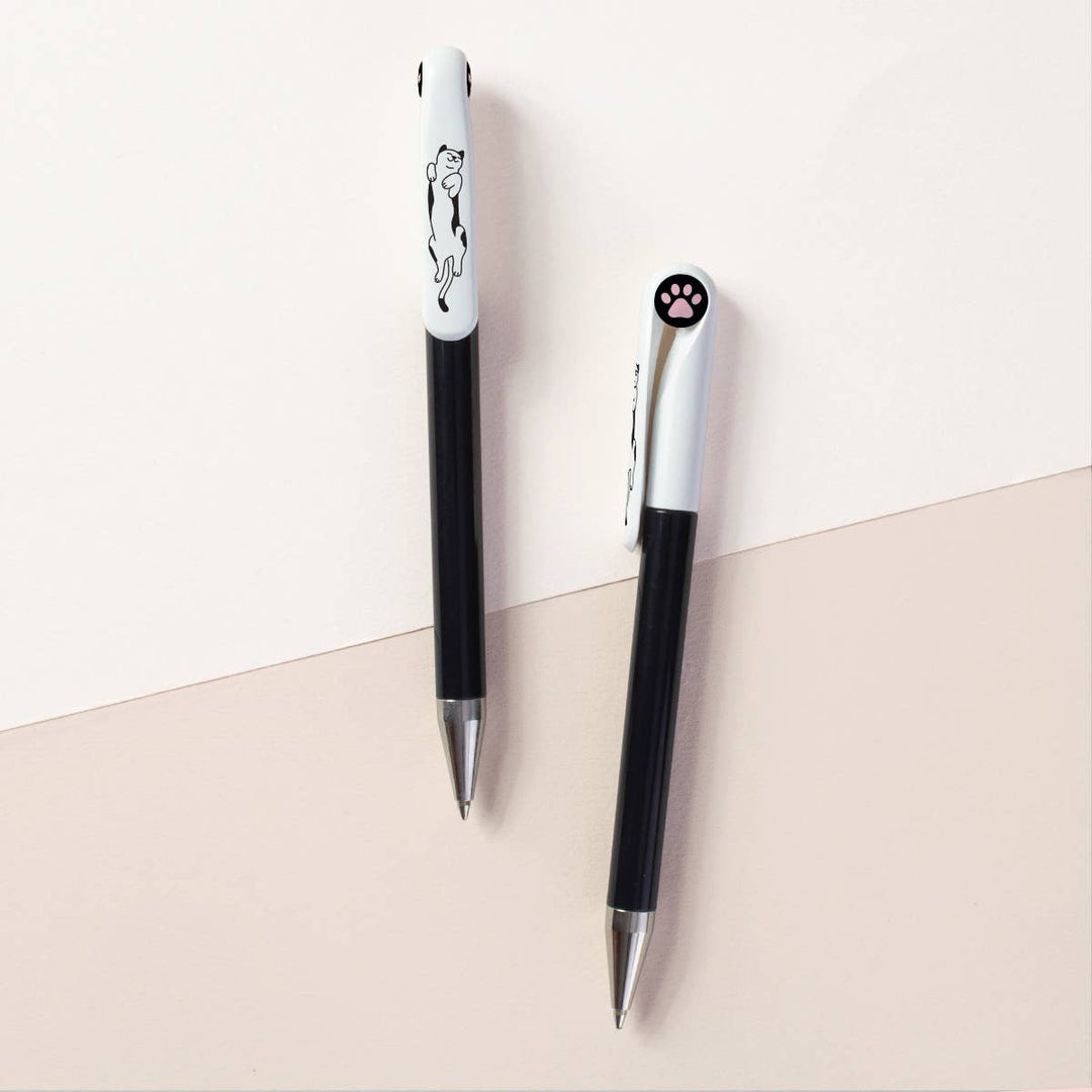 Two sides of a black barrel with white top retractable ballpoint pen with silver tips. One side shows a lounging cat, and the other side has a circular black cap insert with an image of a cat's paw.