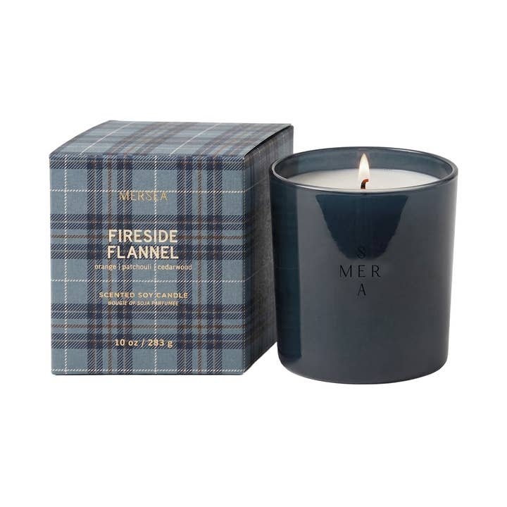 Mersea Fireside Flannel scented soy candle in a dark navy blue glass jar next to its plaid packaging box.