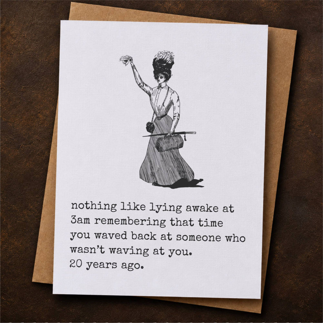 A white greeting card with a black line drawing of a woman in vintage dress and below thatprinted text, placed on top of a brown kraft envelope.