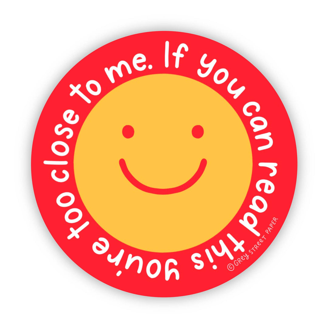 Circular sticker with a yellow smiley face in the center and the text 'If you can read this, you're too close to me" around it in white on a red background.