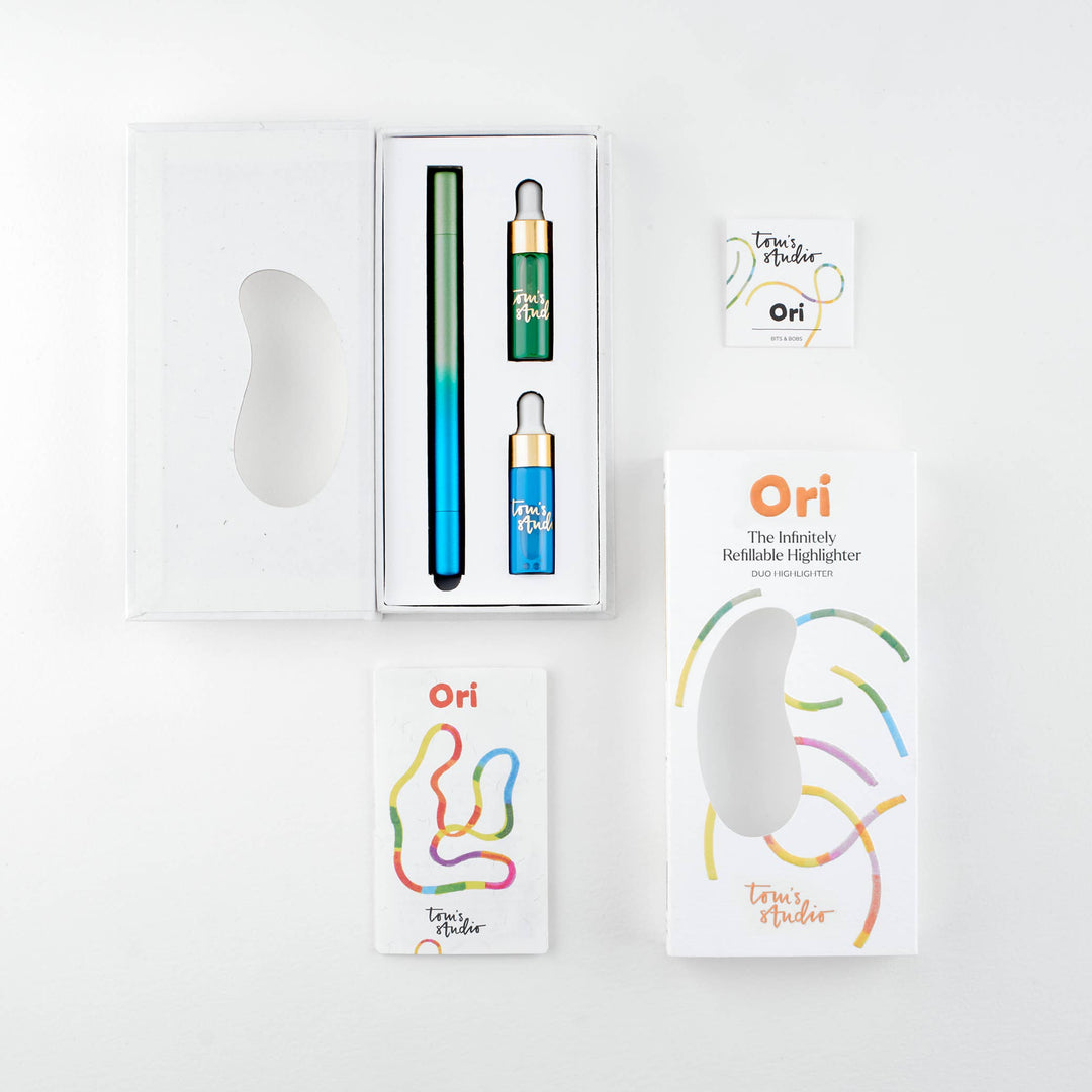 Opened package of the green-blue pen with the pen and two containers of ink next to its cover and a booklet.