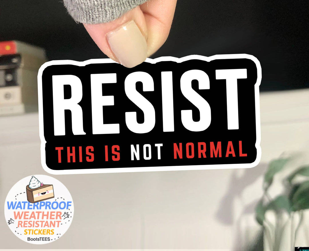 Hand holding a 'RESIST THIS IS NOT NORMAL' sticker with white and red letters on a black background and white border. 