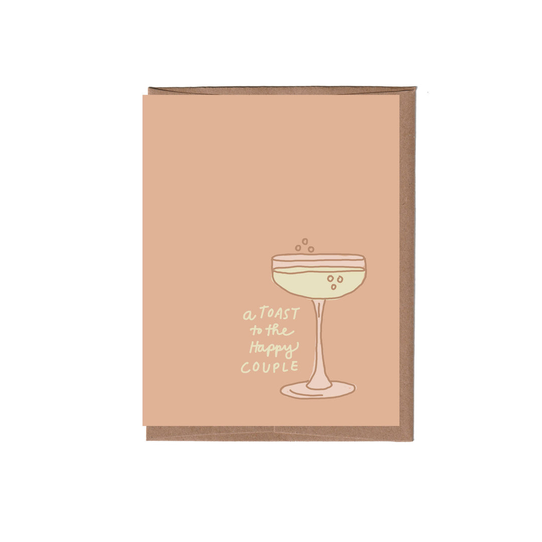 A peach-colored greeting card with a brown kraft envelope, featuring a simple line drawing of a cocktail glass and the text 'A TOAST to the Happy COUPLE'.