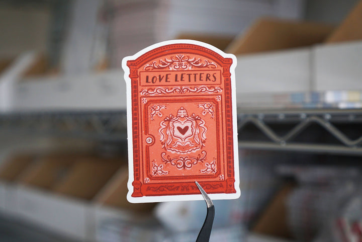 Red card with 'Love Letters' text and heart design on a blurred warehouse background