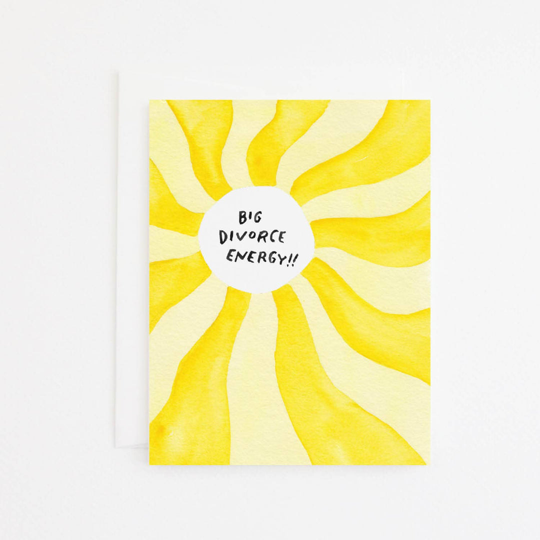 A greeting card with a watercolor-style yellow sunburst design and a white circle in the center that reads 'BIG DIVORCE ENERGY!!' in black handwritten text, shown with a white envelope behind it.