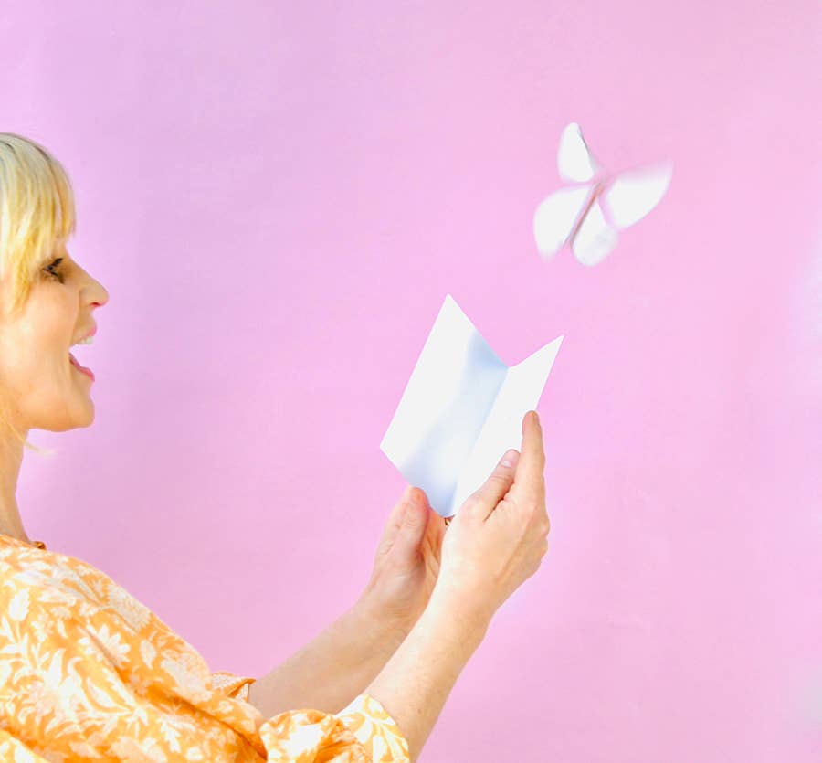 Woman holding an open card with a butterfly flying above it.