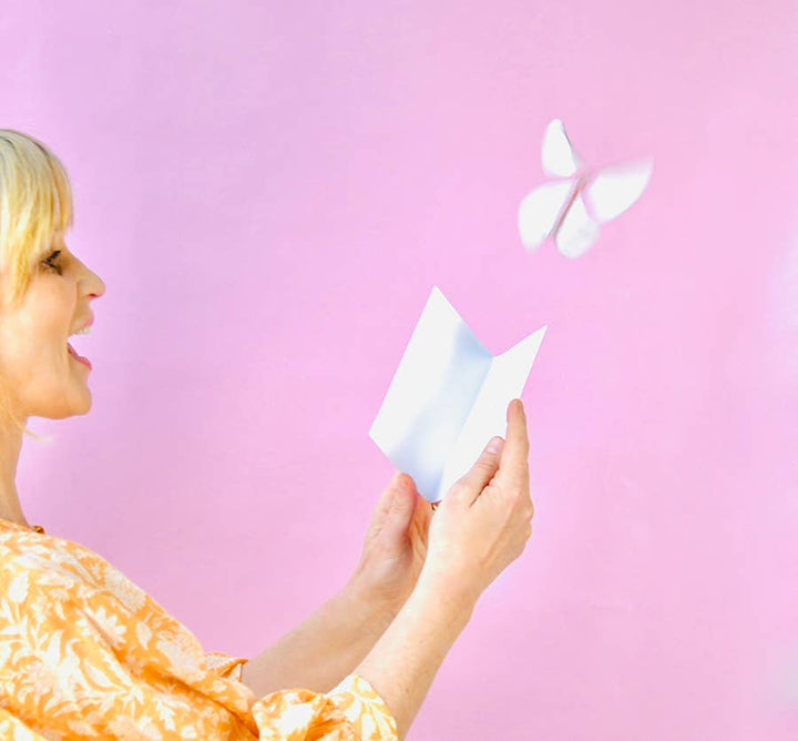 Woman holding an open card with a butterfly flying above it.