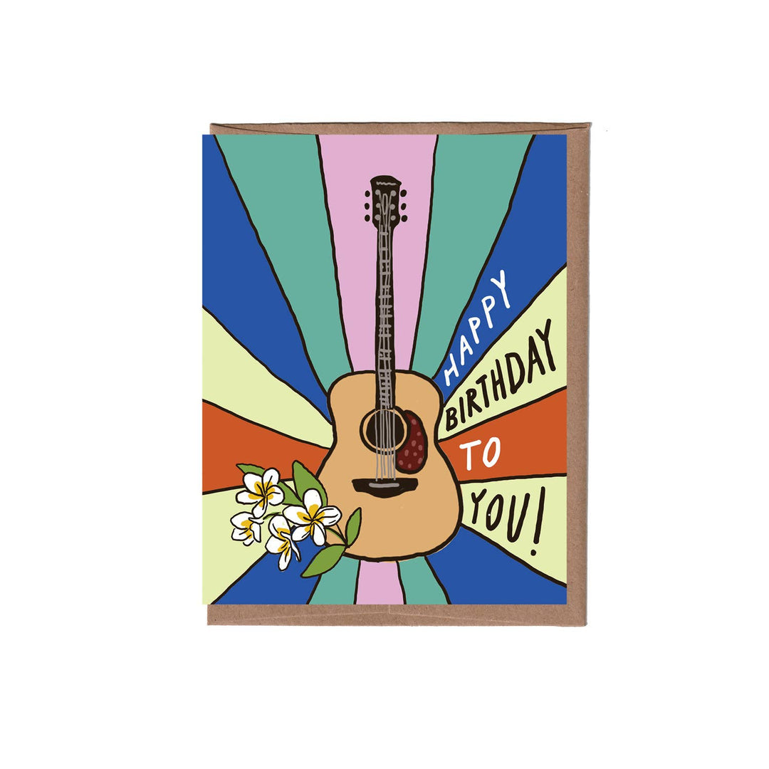 A greeting card with a kraft brown envelop, featuring a colorful retro design with a central acoustic guitar, plumeria flowers, and the text 'HAPPY BIRTHDAY TO YOU!'