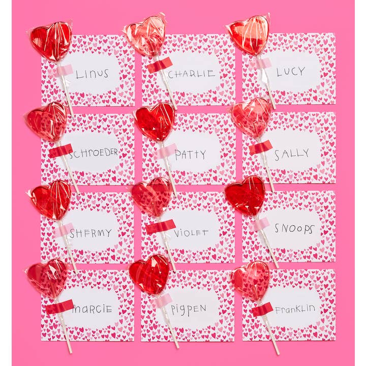 12 envelopes covered in red hearts with a blank white center, addressed in a child's handwriting, with a red lollipop taped to each envelope.
