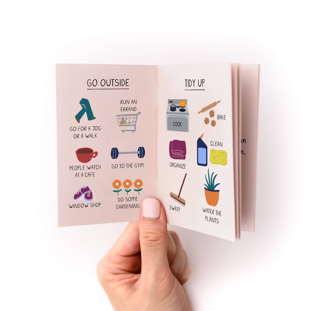 Hand holding a small book with illustrated pages titled 'Go Outside' and 'Tidy Up' with several examples of each.