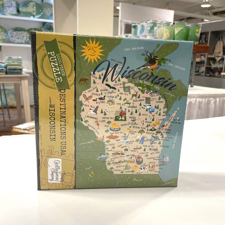 Box of puzzles with image of the state of Wisconsin, showing edges of Lakes Superior and Michigan and bordering states, dotted with city names and local images.