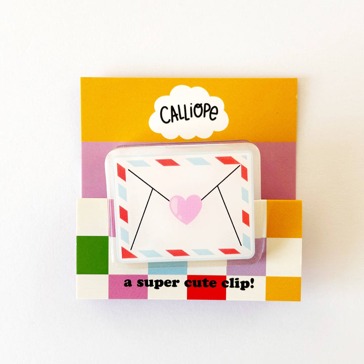 A plastic clip in the image of an airmail envelope with a pink heart on it. The words "a super cute clip!" appear on packaging material along with the word CALLIOPE