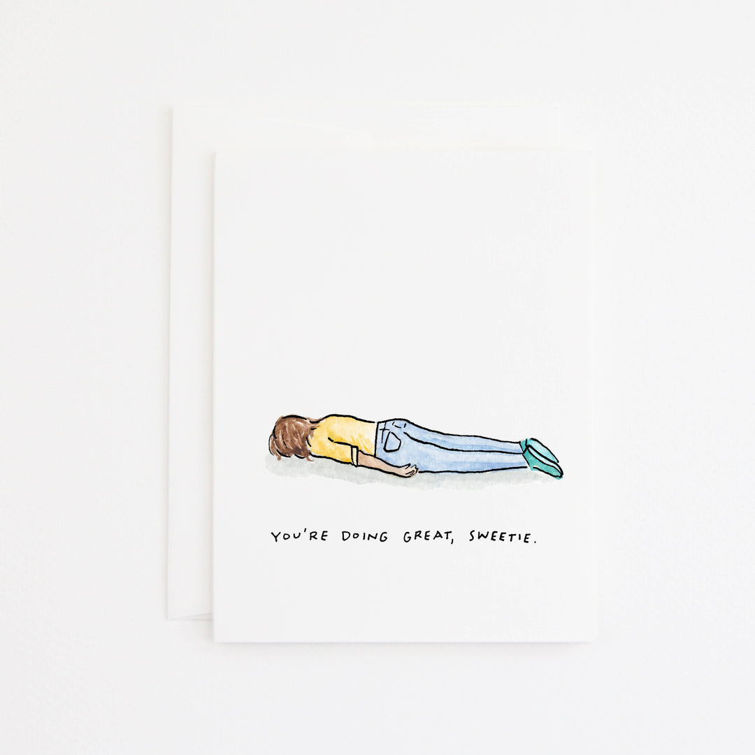 A white greeting card with a hand-drawn illustration of a person lying flat on their face, wearing a yellow shirt and blue jeans, with the text 'YOU'RE DOING GREAT, SWEETIE.' below.