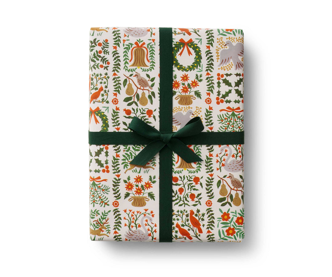 Giftwrapped box  in holiday pattern of wreaths, pears, cardinals, and florals on a white background, and tied with a green ribbon.