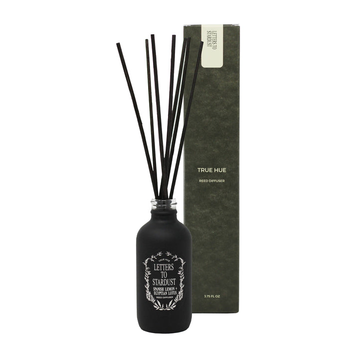 True Hue Letters to Stardust diffuser in a black bottle with white lettering, with seven reeds inserted, next to its black box.