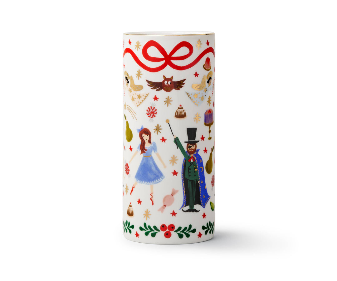 Cylindrical vase with Nutcracker illustrations, a red ribbon at the top, and holly at the bottom, on an off-white background.