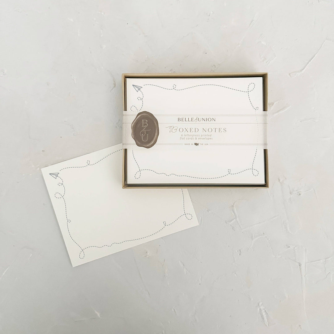 A boxed set of white stationery notes with a gold-toned frame, a white ribbon band, and a brown wax seal featuring the initials 'BA.'