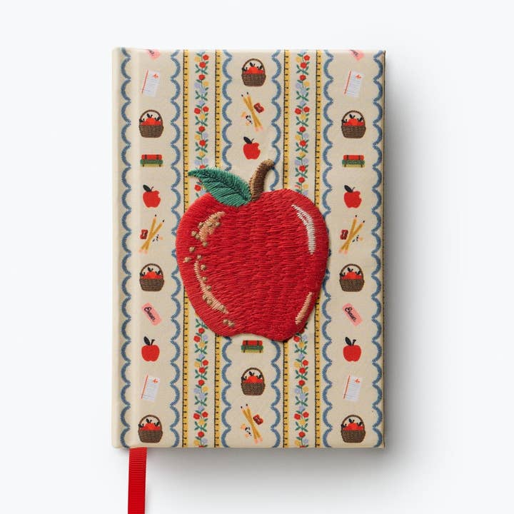 Cover of notebook with background pattern of school-related objects with an embroidered large apple in the center.