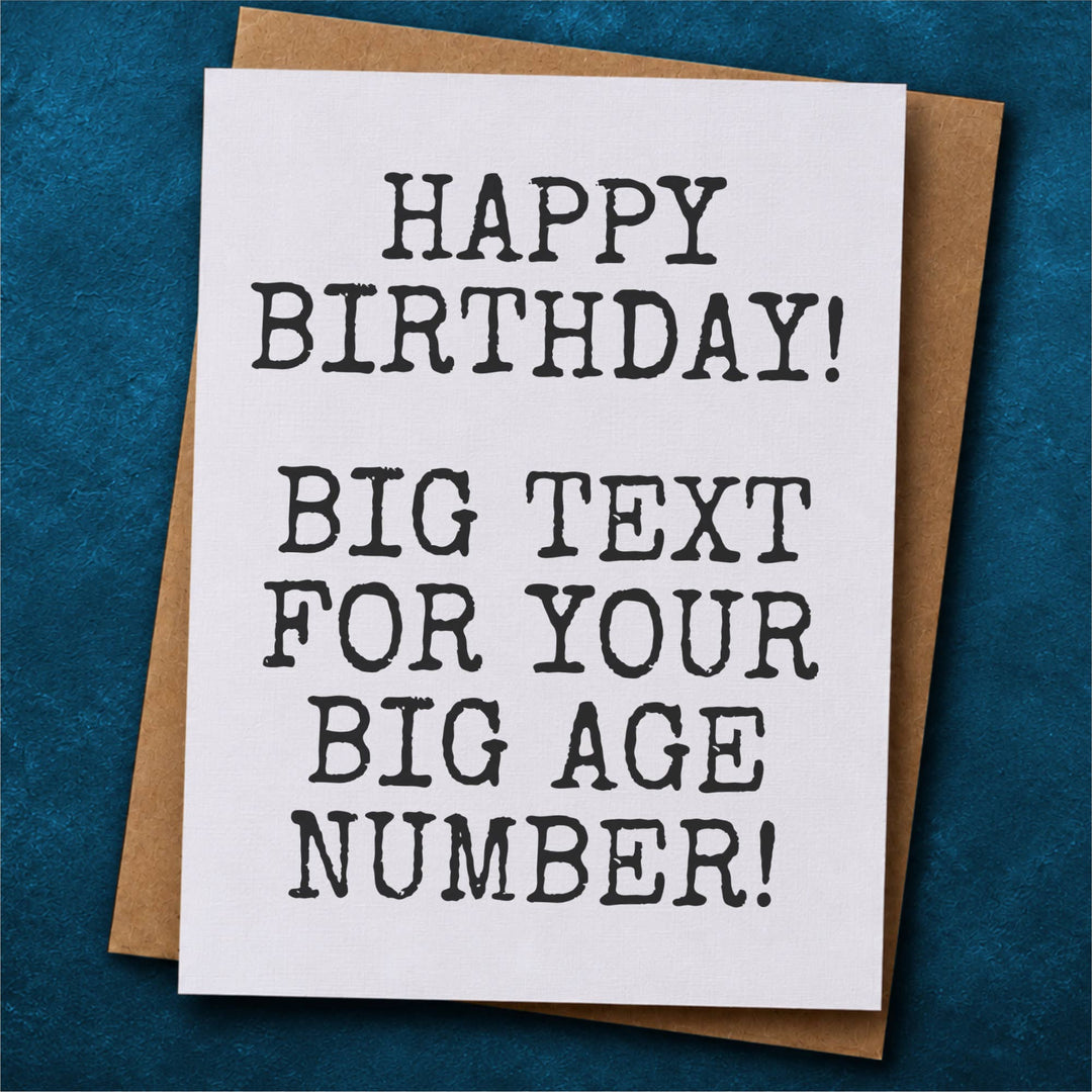 A white greeting card with bold black text reading 'HAPPY BIRTHDAY! BIG TEXT FOR YOUR BIG AGE NUMBER!' placed on top of a brown envelope.