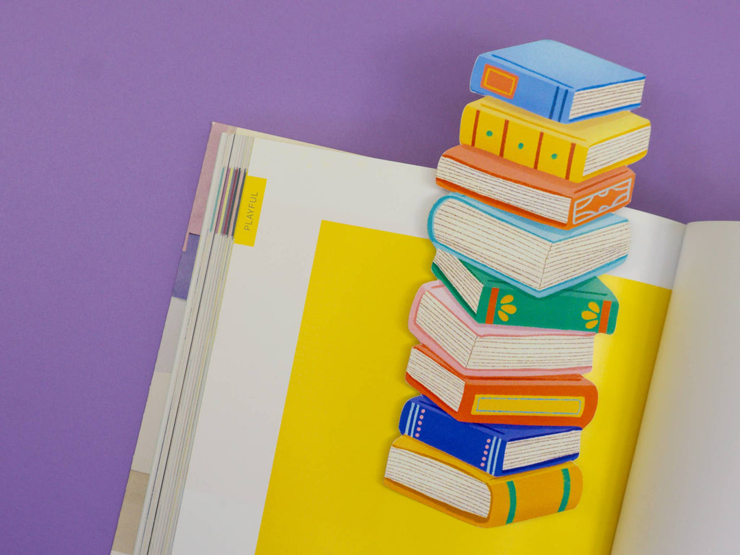 Bookmark in the shape of a stack of nine books, each a different color, on the page of an open book.