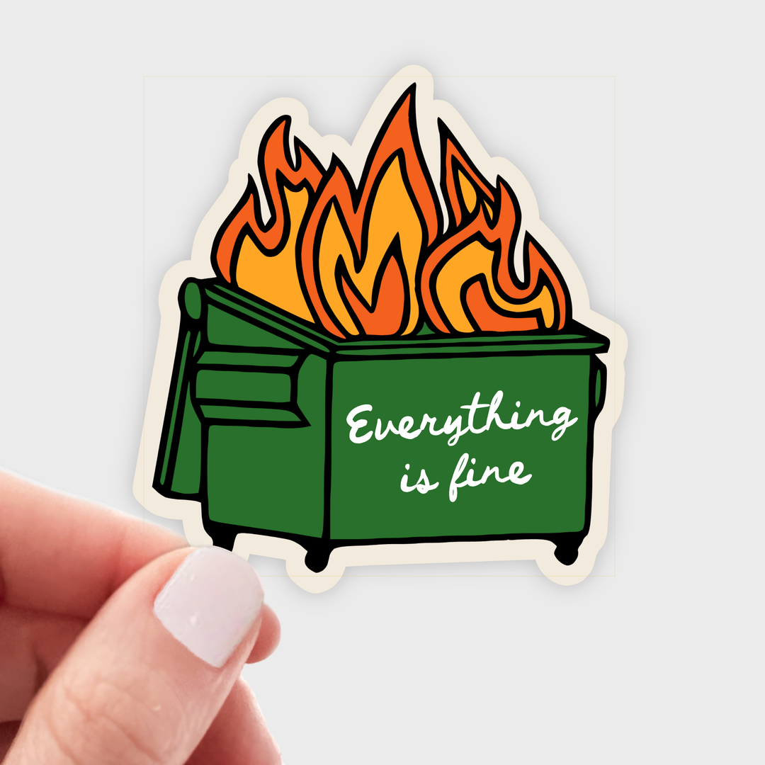 Hand holding a sticker of a burning green dumpster with the text 'Everything is fine'