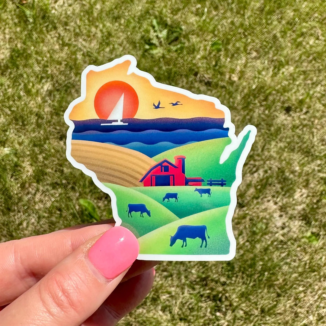 Sticker shaped like the state of Wisconsin, featuring a colorful rural landscape with a red barn, blue cows, green hills, blue water with sailboat, and a yellow-orange sunset.