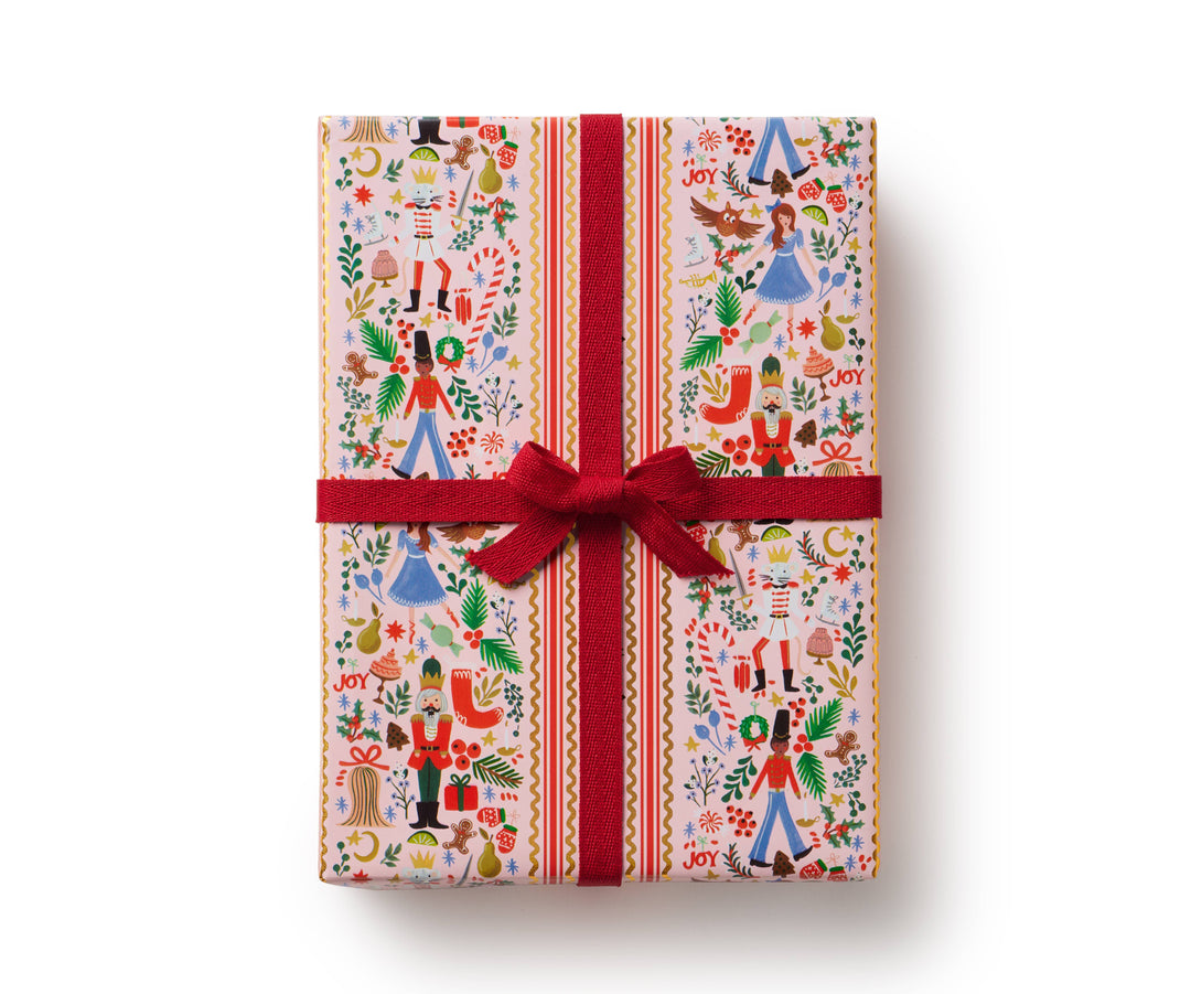 Gift box wrapped in light-colored Nutcracker-themed paper and a red ribbon.
