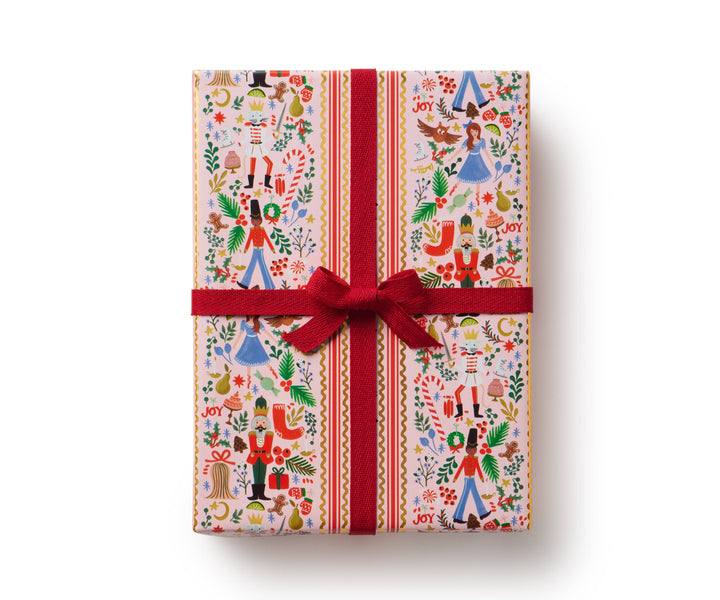 Gift box wrapped in light-colored Nutcracker-themed paper and a red ribbon.