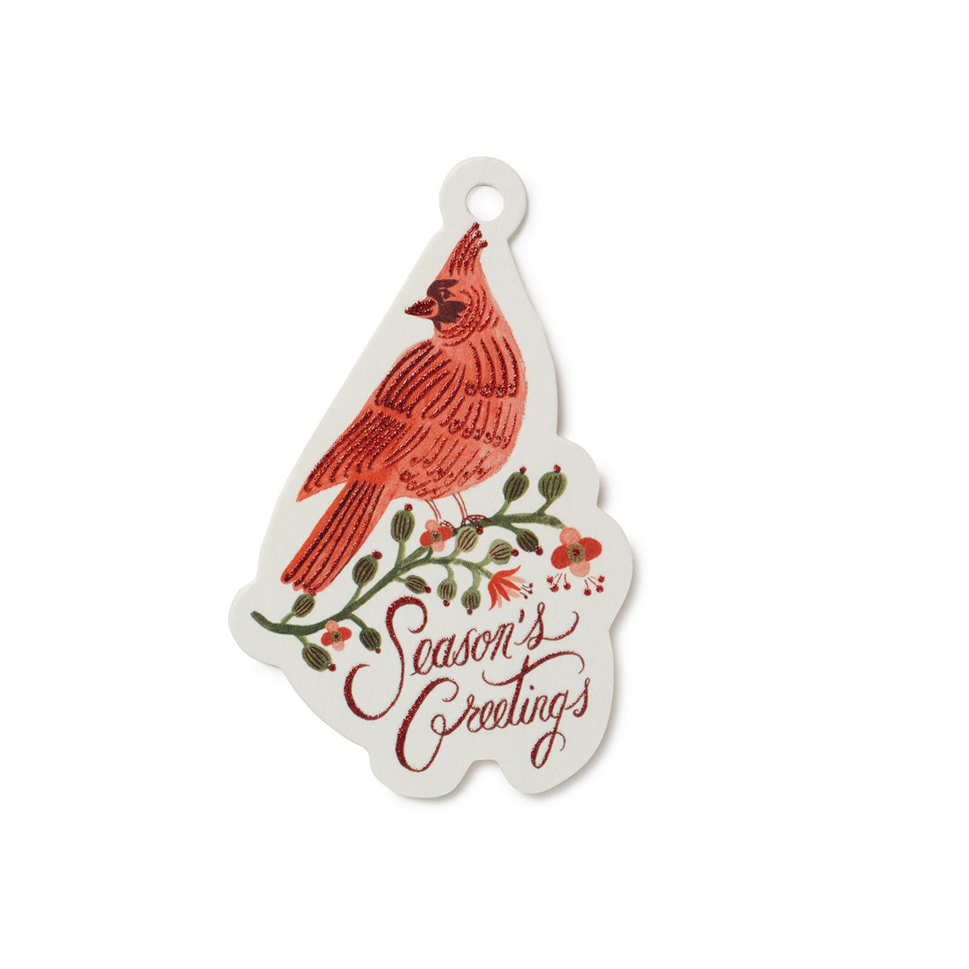 A white Christmas gift tag shaped like a pine tree, featuring an illustration of a cardinal perched on a branch with the words 'Season's Greetings' in red script.