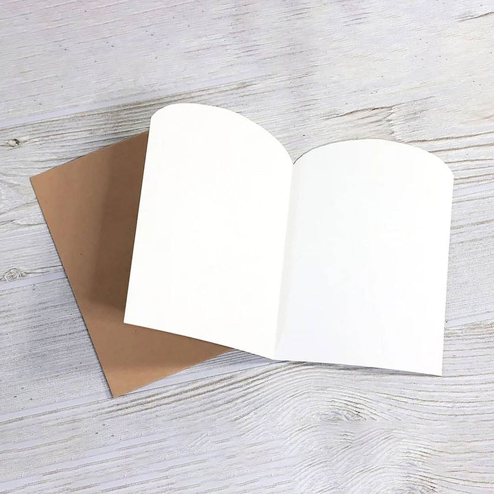 Blank card open to show die-cut arched top next to brown kraft envelope.