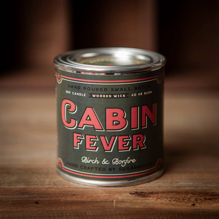 Soy candle in tin. Green label with red lettering. Label is Cabin Fever Birch and Bonfire.