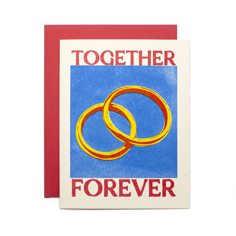 A greeting card with a red envelope behind it, featuring the words 'TOGETHER FOREVER' in red around a blue central panel with two interlocking gold rings.
