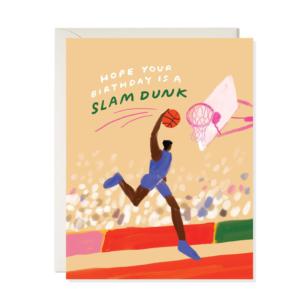A greeting card with a basketball-themed illustration and the text 'HOPE YOUR BIRTHDAY IS A SLAM DUNK,' shown with a white envelope behind it on a light gray background.