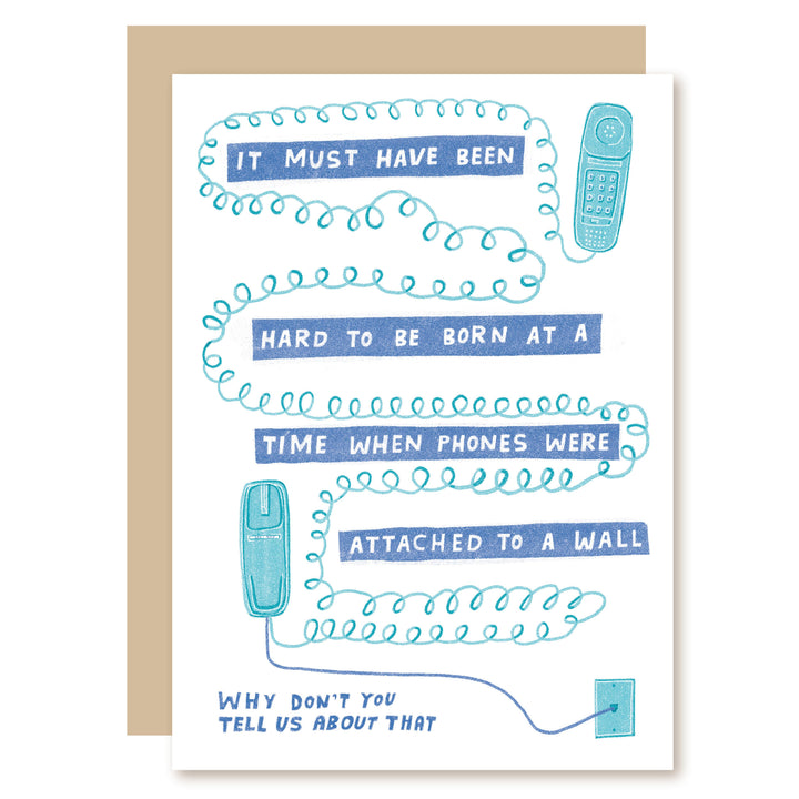 A humorous greeting card with a kraft envelope, featuring a hand-drawn blue coiled phone cord and illustrations of old wall phones with text that reads, 'IT MUST HAVE BEEN HARD TO BE BORN AT A TIME WHEN PHONES WERE ATTACHED TO A WALL' and 'WHY DON'T YOU TELL US ABOUT THAT'.