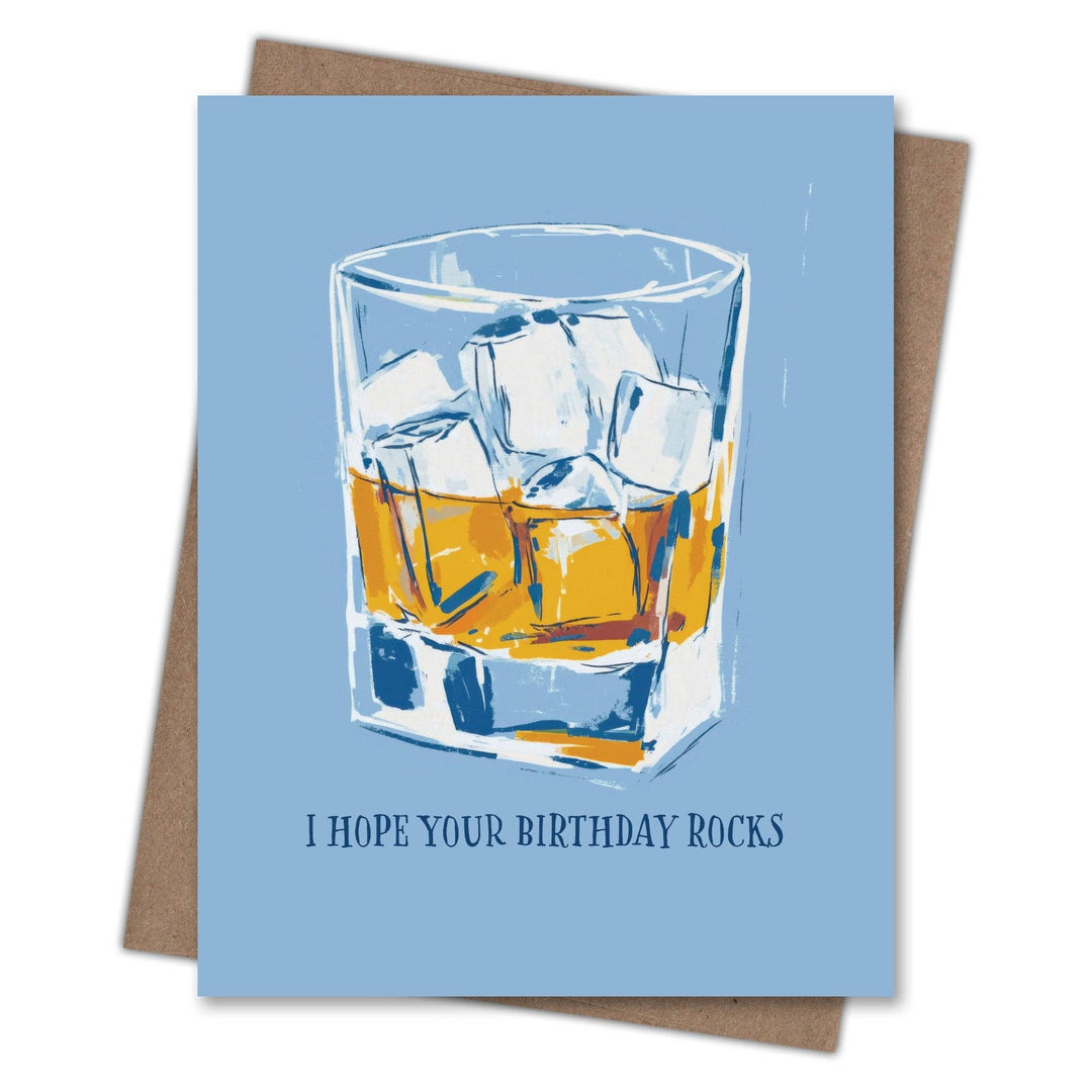 Greeting card with a glass of whiskey and ice cubes on a blue background, featuring the text 'I hope your birthday rocks'.