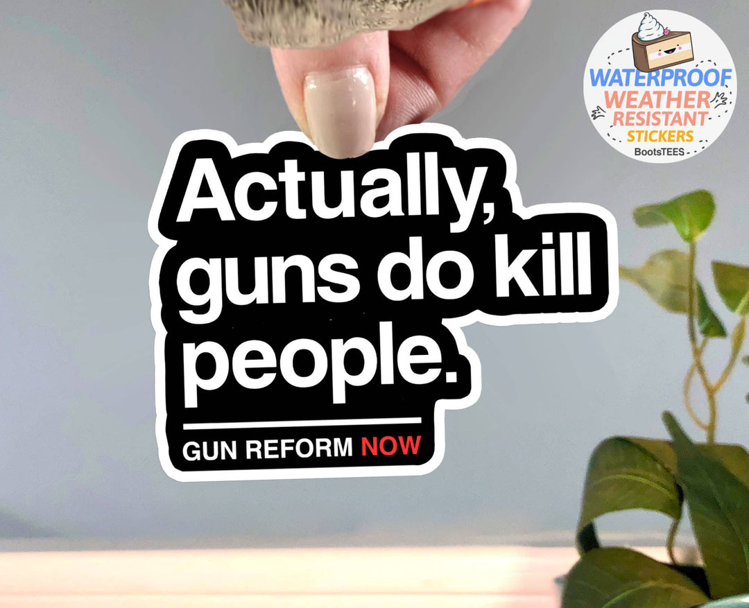 A hand holds a die-cut sticker with the text 'Actually, guns do kill people. GUN REFORM NOW' in white lettering on a black background with a white border.