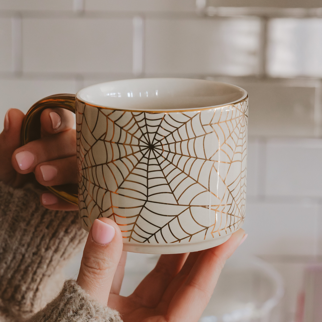 Person holding a mug with spider web design, gold handle and gold rim.