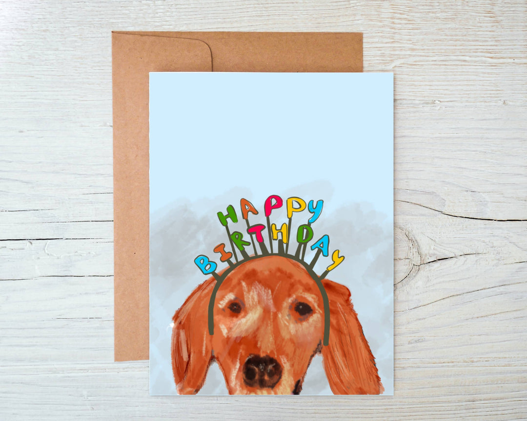 Front of card with the head of a golden retriever wearing a headband spelling 'happy birthday' on a white background.