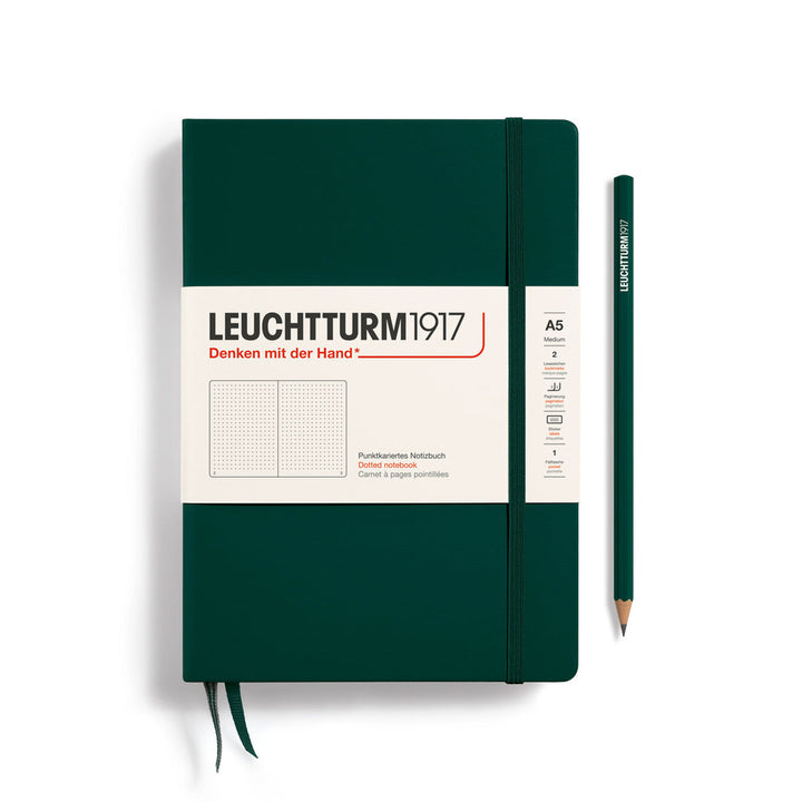A Leuchtturm1917 A5 hardcover dotted page notebook in forest green with a white label on the front, shown closed with an elastic closure and ribbon bookmark. A matching forest green pencil is placed vertically to the right.