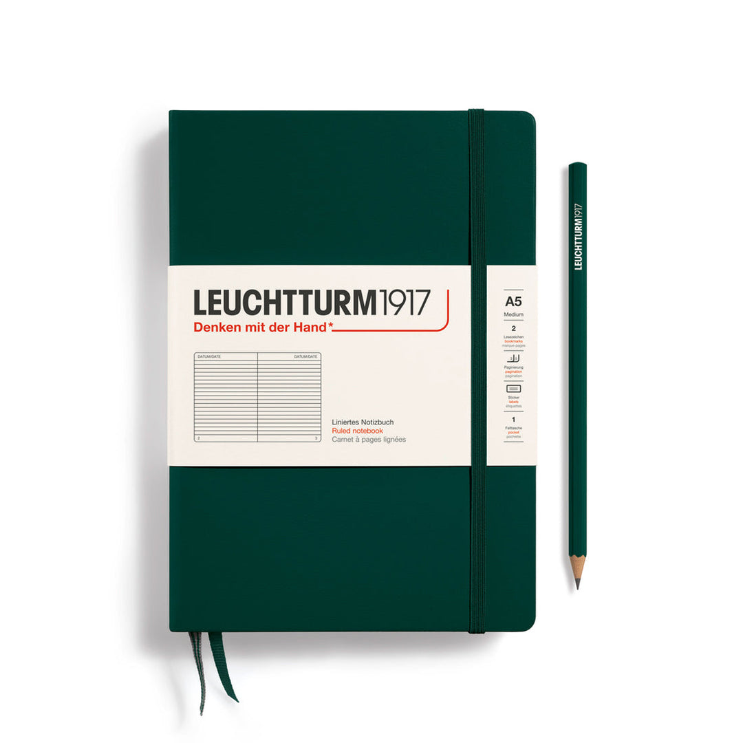 A Leuchtturm1917 A5 hardcover ruled page notebook in forest green with a white label on the front, shown closed with an elastic closure and ribbon bookmark. A matching forest green pencil is placed vertically to the right.