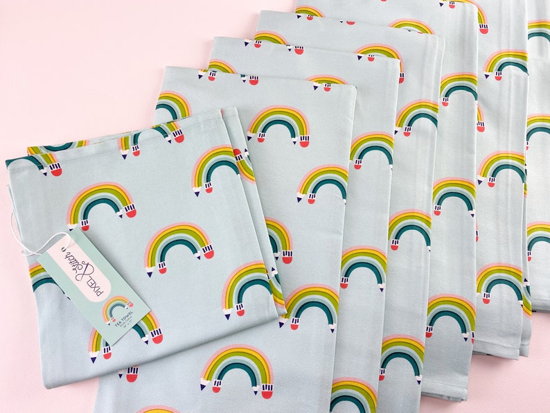 Set of colorful rainbow-patterned kitchen towels with pencils  arced to appear as a rainbow on a light blue background.